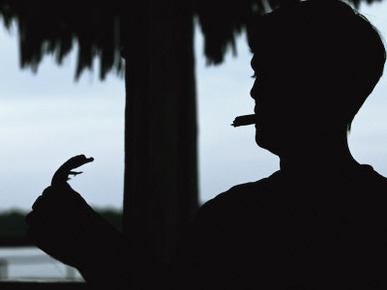 A Cigar-Smoking Cuban Man in Silhouette Holds a Baby Crocodile